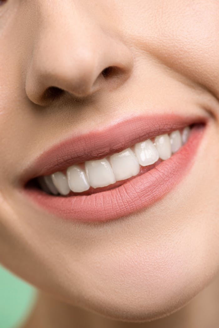A close-up image focusing on a womans smiling mouth, showing white teeth and pink lips.